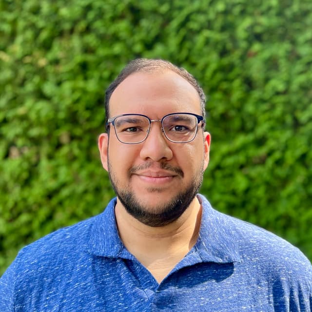 Portrait photo of Kapil Garg. He is a tall Indian man with short black hair and a beard. He is wearing square glasses and a blue polo shirt.